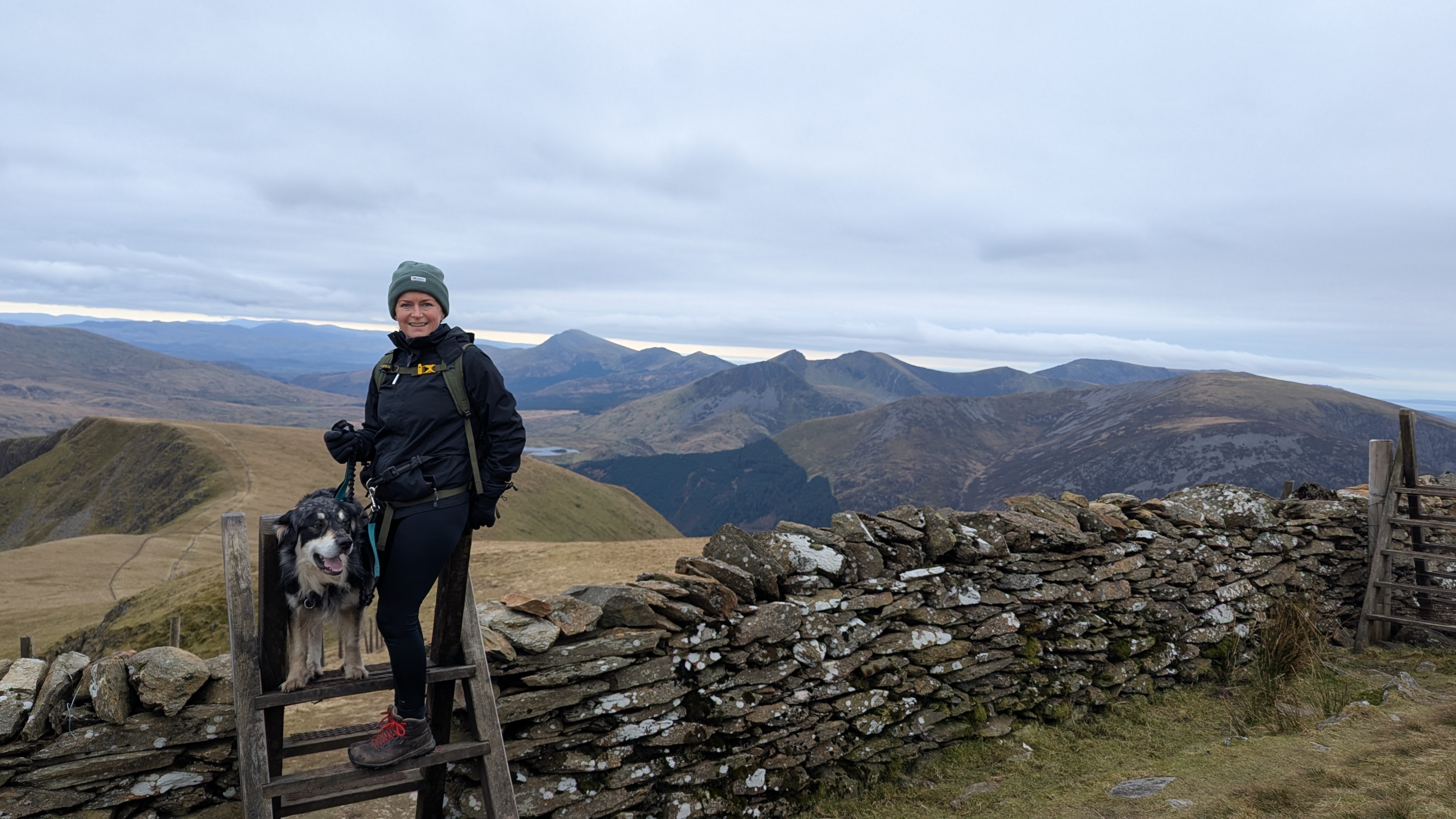 on a stile on the descent from Moel Eilio with the Nantlle ridge and mynydd mawr in the background