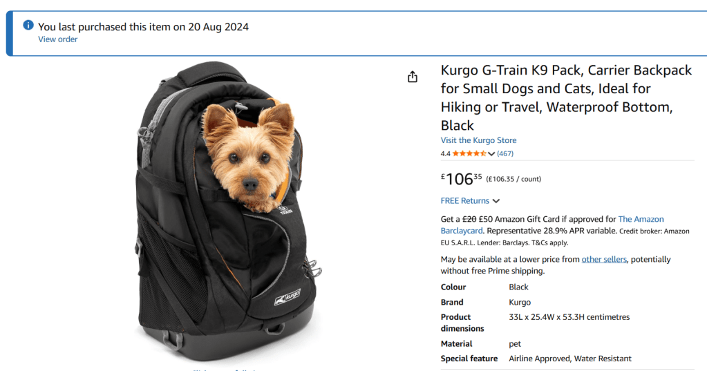 A small dog peeking out of a black pet carrier backpack designed for hiking and travel.