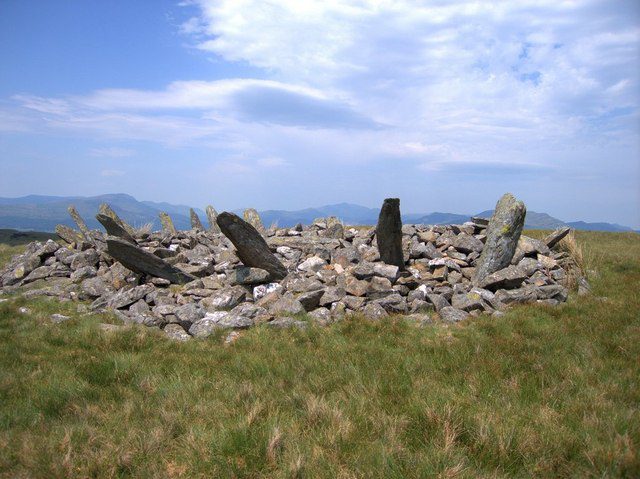 Ancient stone circle surrounded by grass, featuring upright stones and a low mound.