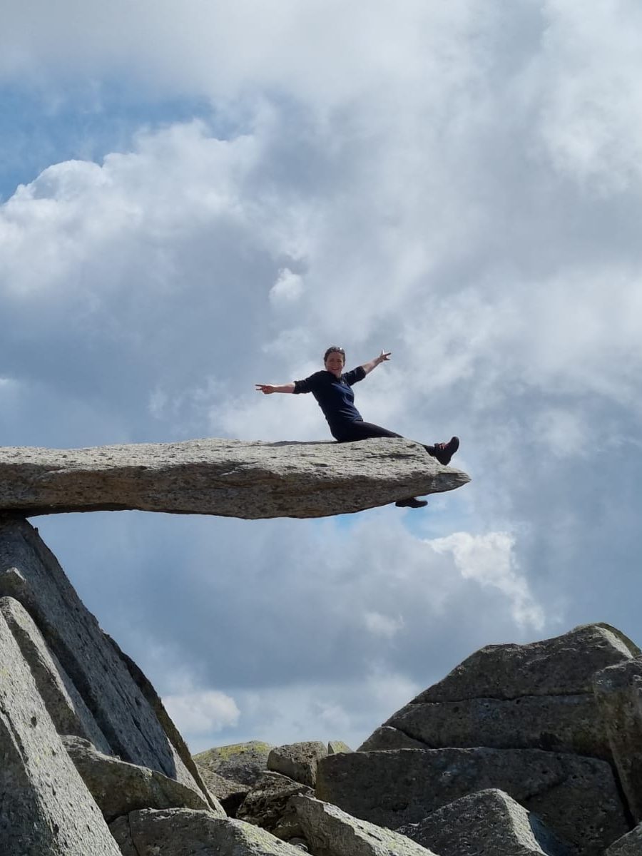 Two people posing on a rock outcrop with dramatic clouds in the background.
