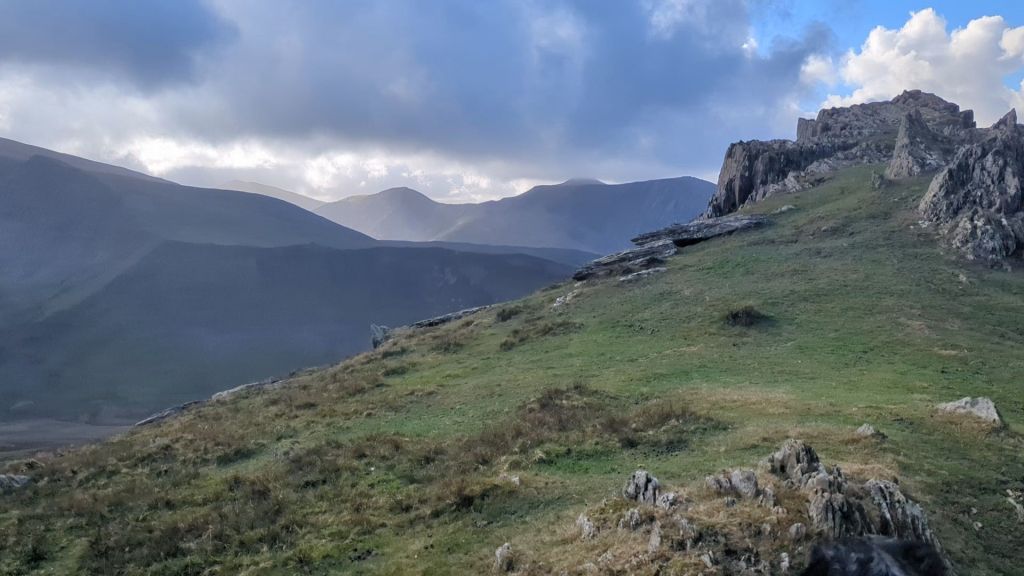Scenic view of the North East Ridge of Yr Elen, featuring rocky outcrops and grassy slopes under a cloudy sky.