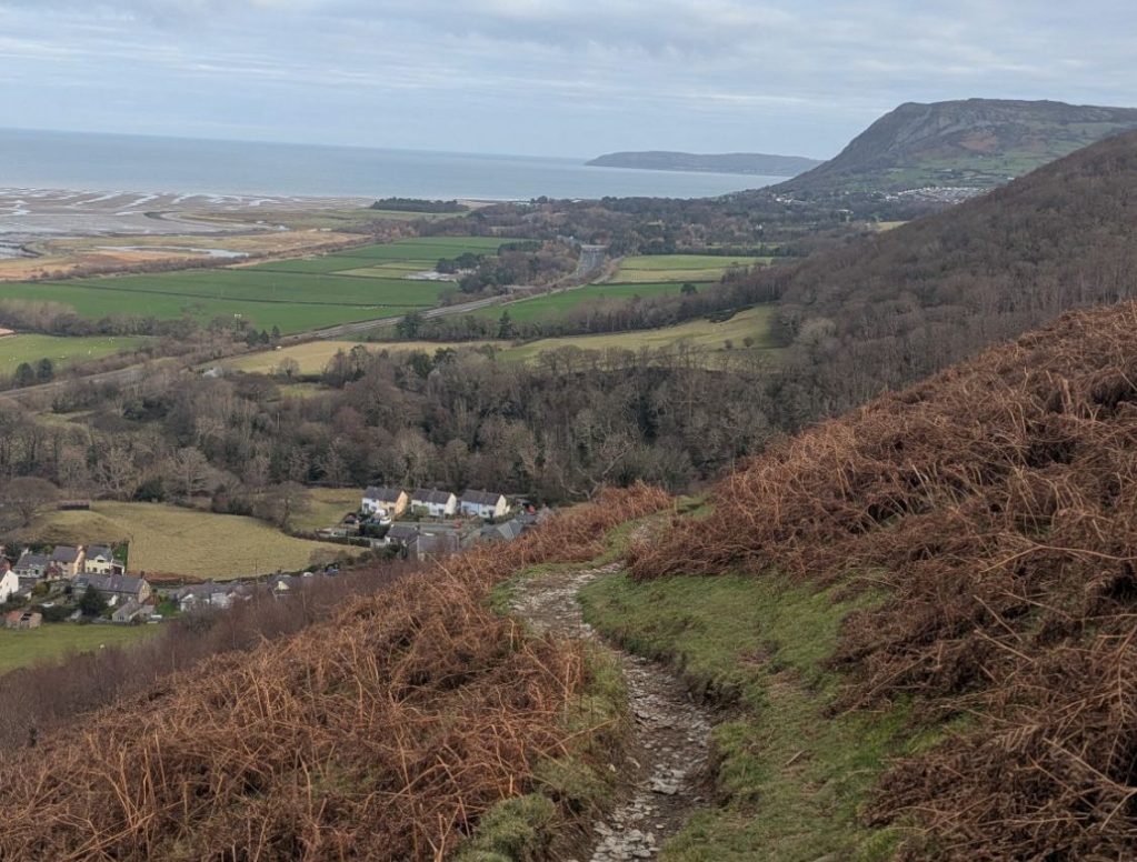 A scenic view from Bera Bach overlooking the coastal landscape of North Wales, with fields and villages in the foreground, leading to the sea in the background.