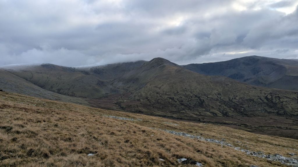 View of the Carneddau mountains from Bera Bach, showcasing rolling hills and a cloudy sky.
