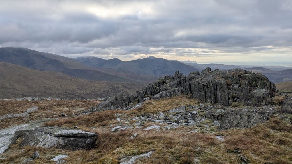 Rocky summit of Bera Bach with panoramic views of rolling hills and mountains under a cloudy sky.