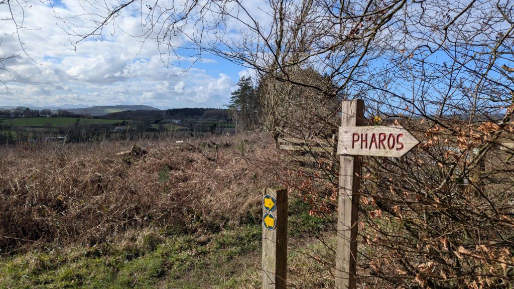 A wooden signpost indicating 'Pharos' with a right arrow, set against a backdrop of rolling hills and a partly cloudy sky.