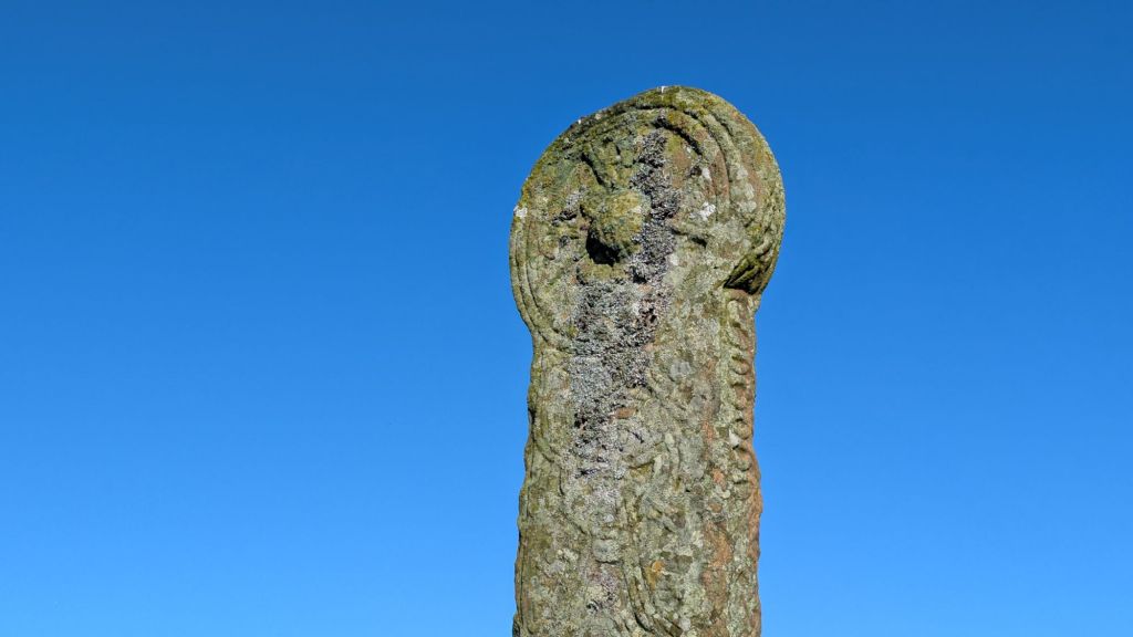 A close-up of an ancient stone monument covered in moss and lichen, set against a clear blue sky.