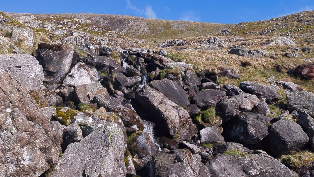 Rocky landscape with large boulders and patches of grass under a clear blue sky.