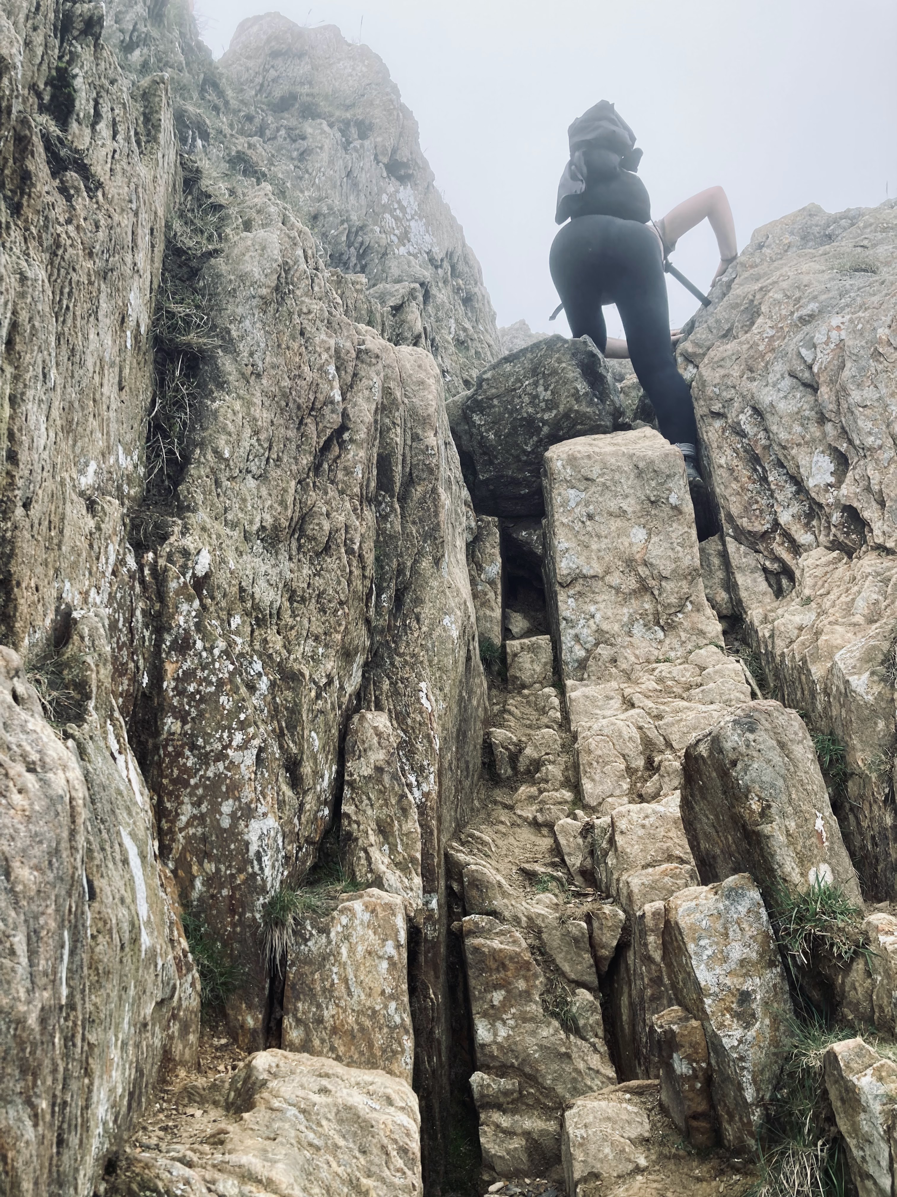 A person climbing rocky terrain with large boulders, shrouded in fog.