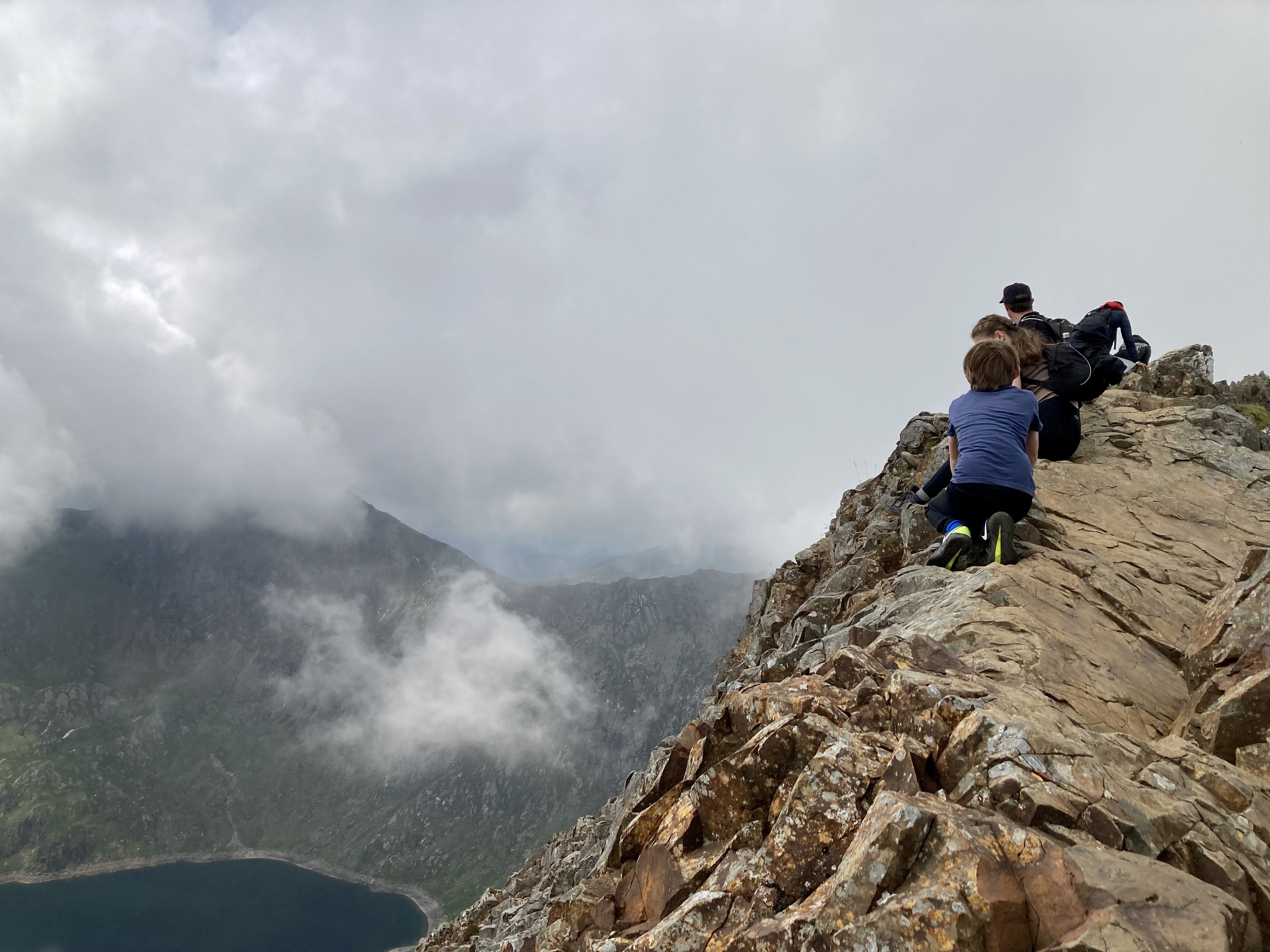 Group of hikers on a rocky mountain ridge with clouds in the background.