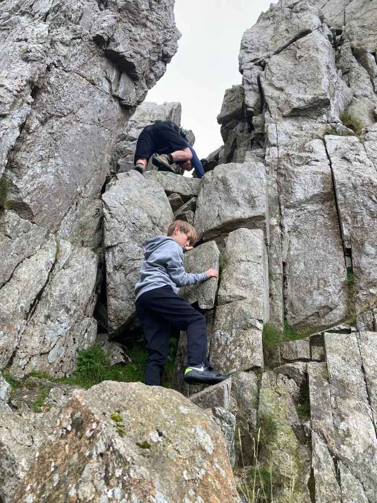 Two children climbing a rocky outcrop in a natural landscape.